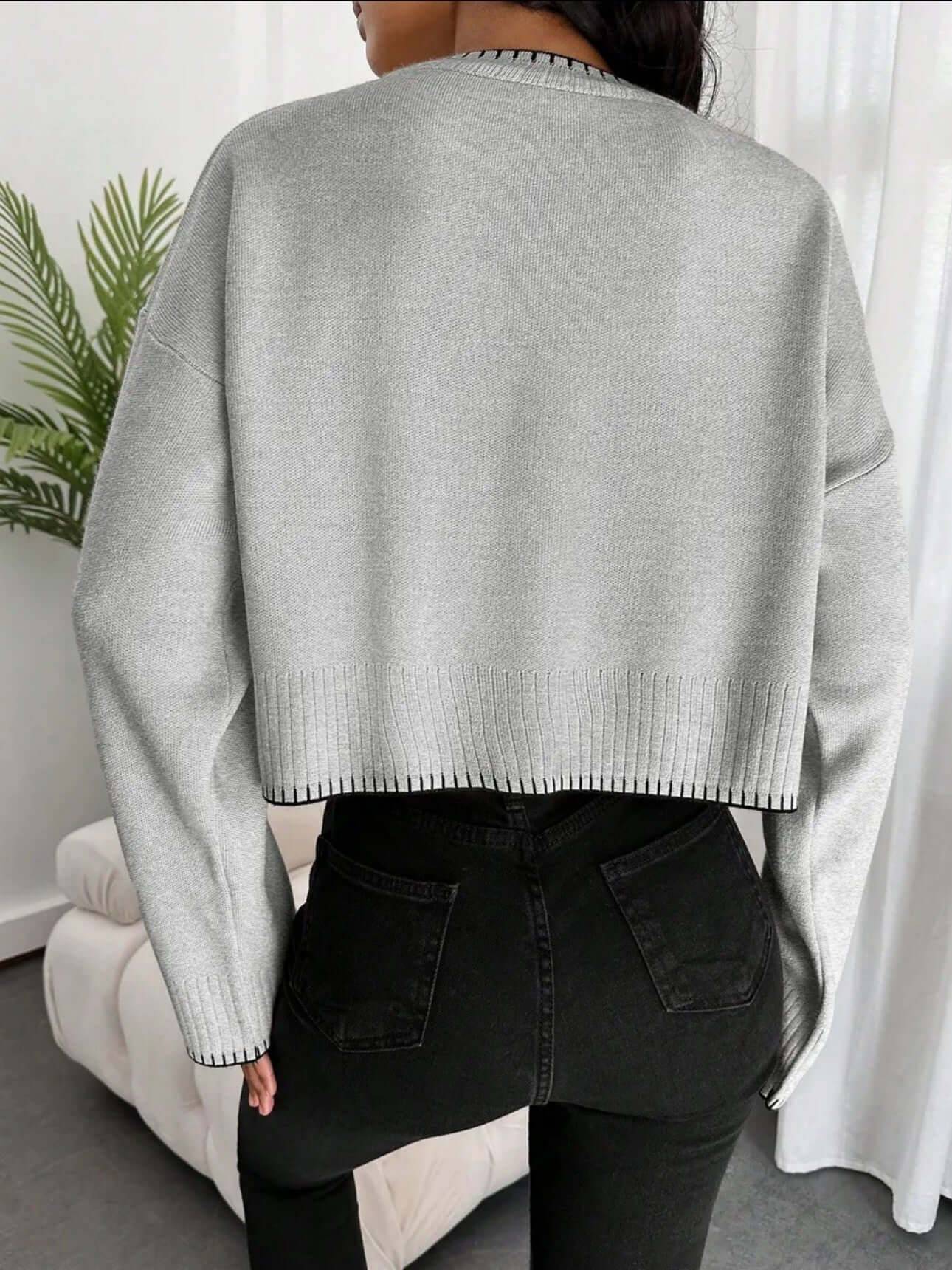 Woman wearing a gray cropped loose sweater OEM with a black trim, showcasing the back style.