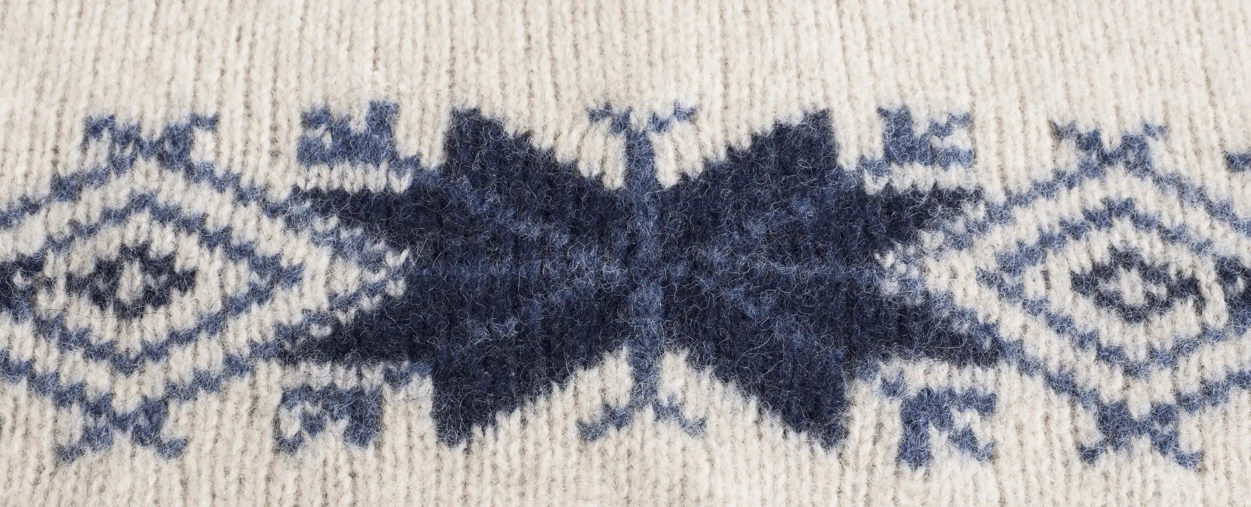 Close-up detail of expert jacquard knitting craftsmanship, featuring our brand promise: Expert Knitwear, Uncompromised Quality.