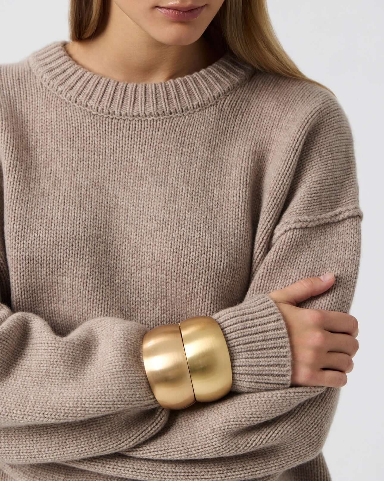 Model wearing a women's long sleeve round neck sweater with drop shoulder and gold bangles.