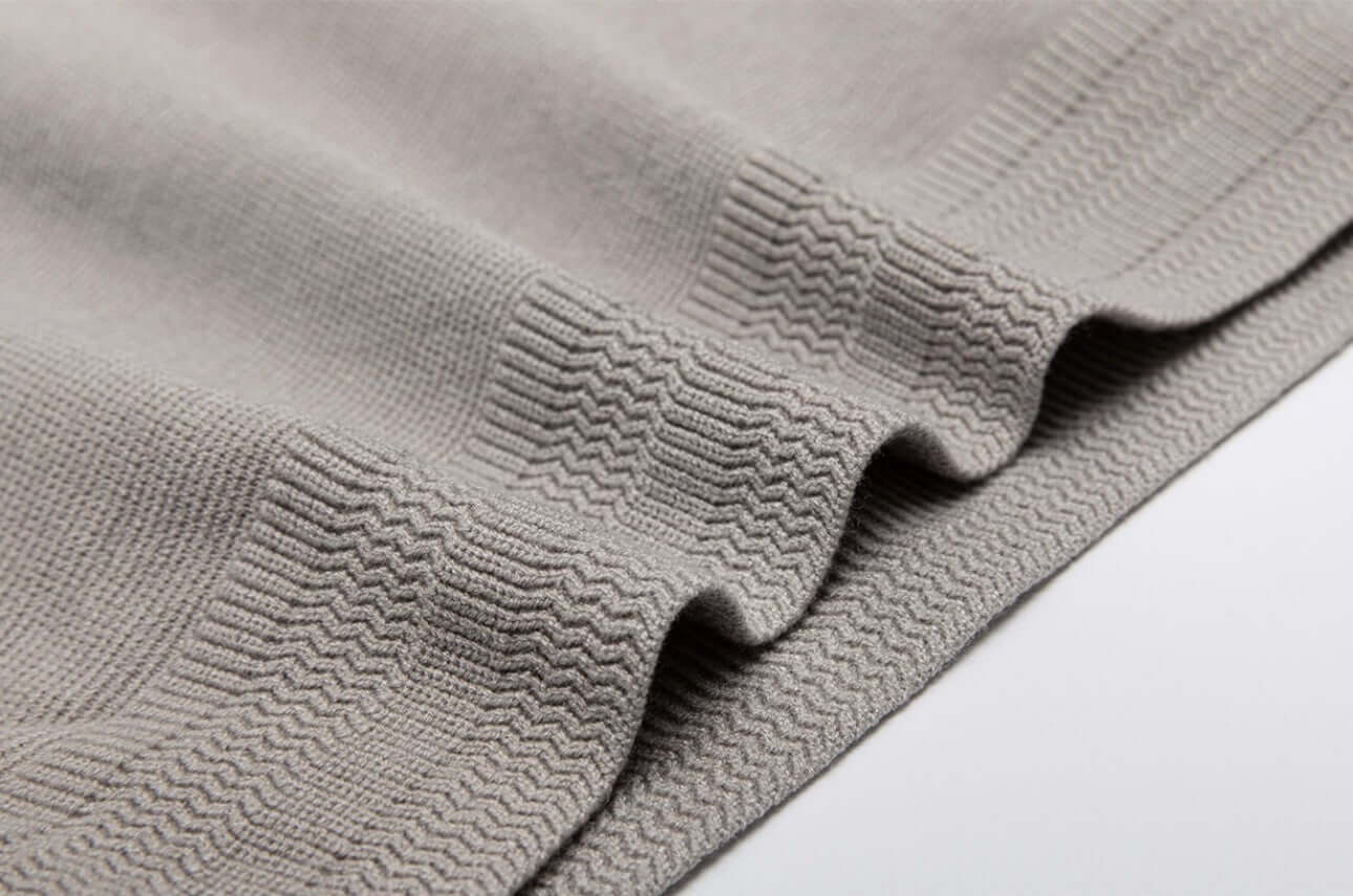 Close-up view of a light gray textured fabric, showcasing the knit pattern of a men's wool sweater OEM.