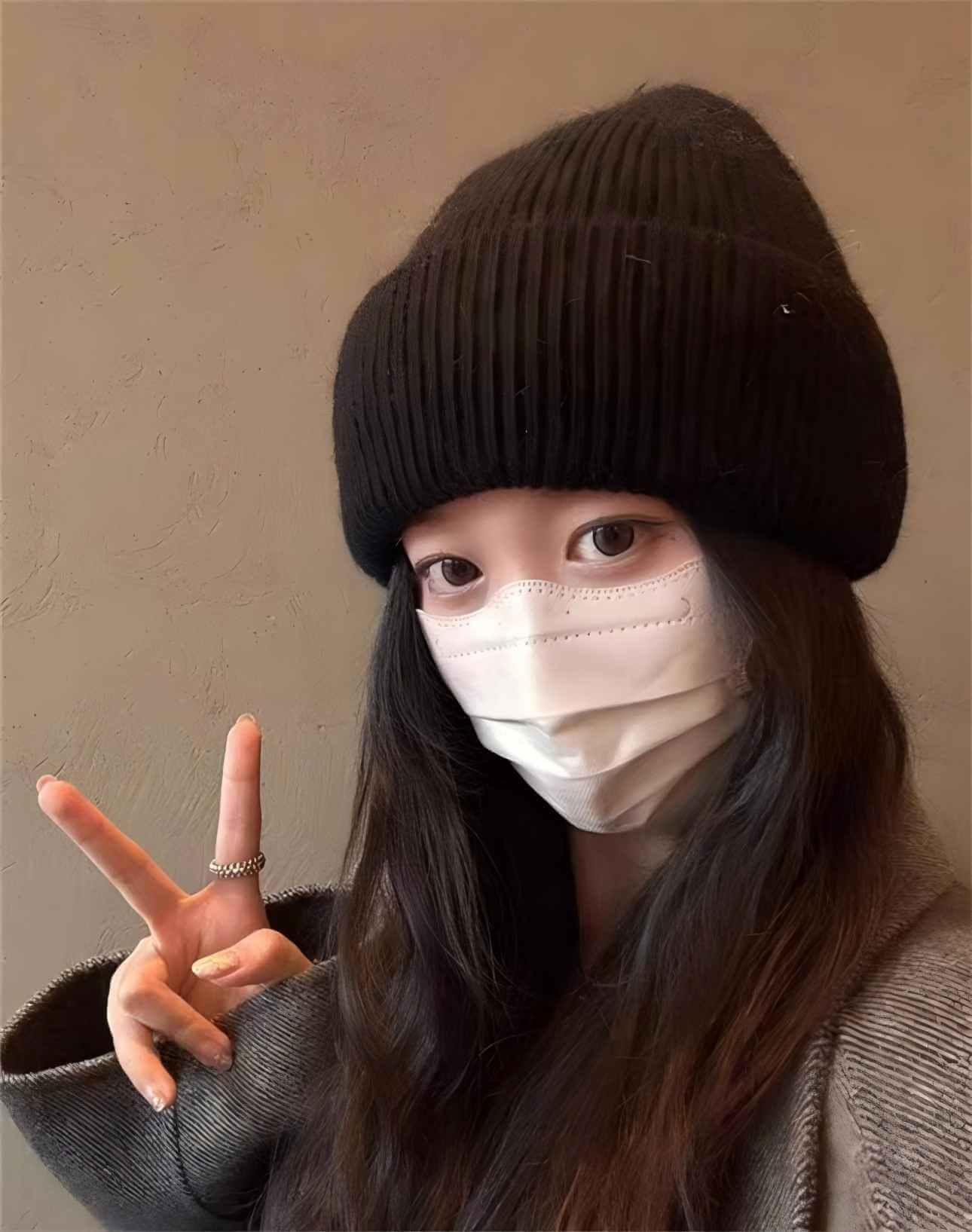Warm Hat OEM | Woman wearing a black rabbit hair beanie with folded brim and face mask, showing peace sign.