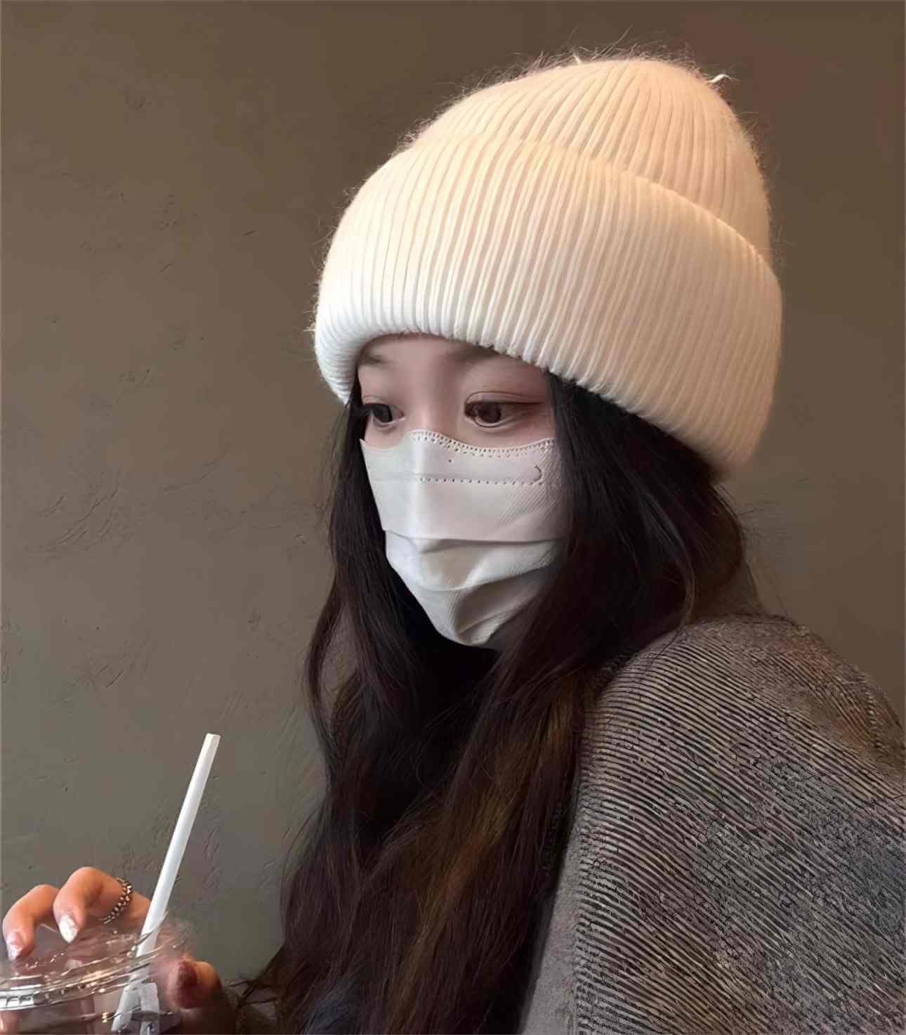 Woman wearing a white ribbed Warm Hat OEM and a face mask while holding a drink.